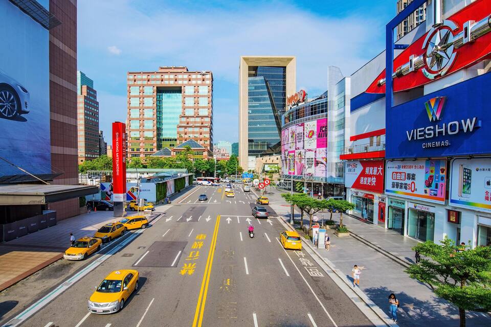 A busy urban street with yellow taxis, pedestrians, and modern buildings including a cinema.