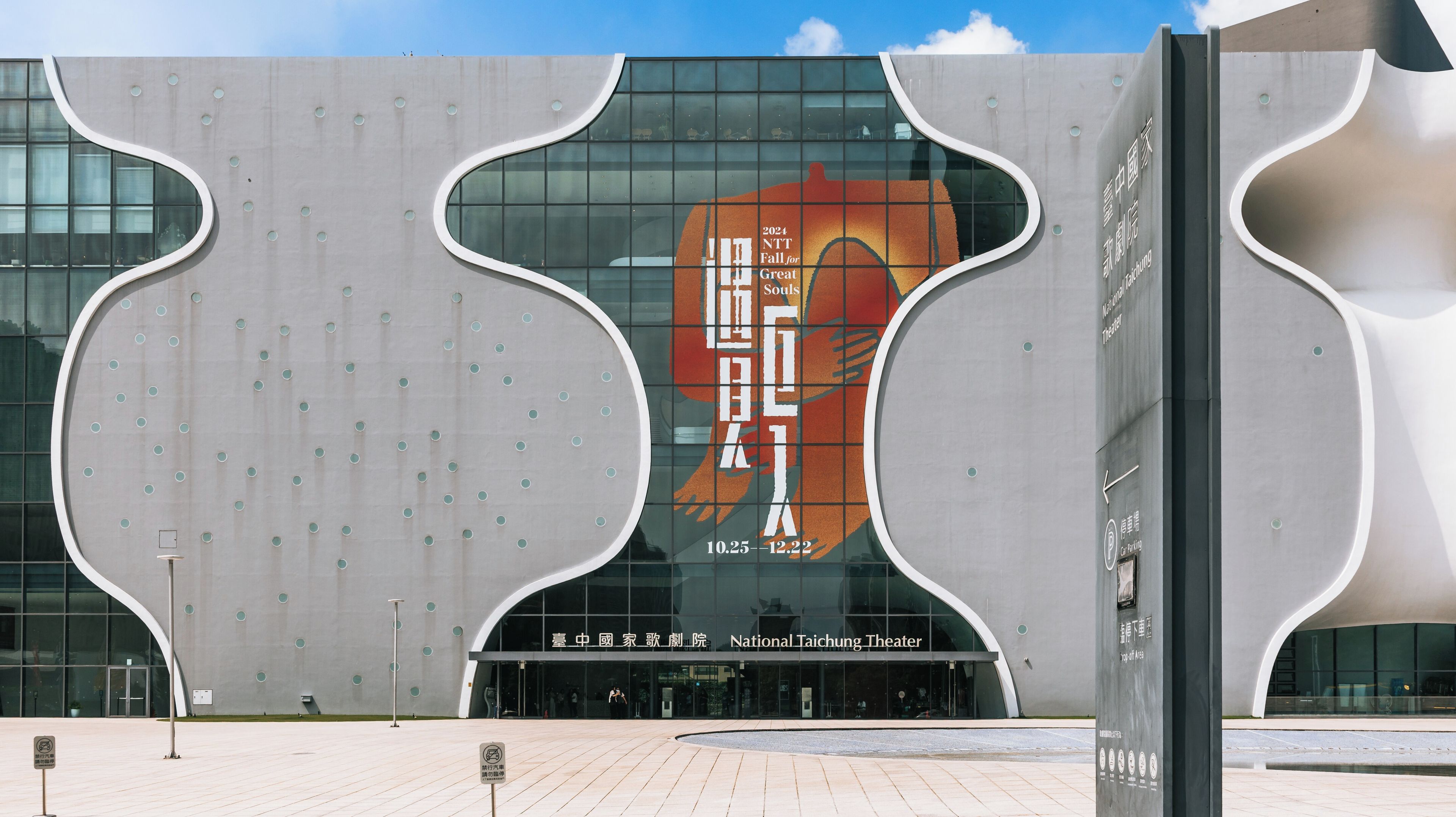 A modern building with a unique curved facade and a large advertisement for the 2024 NTT Fall for Great Souls.
