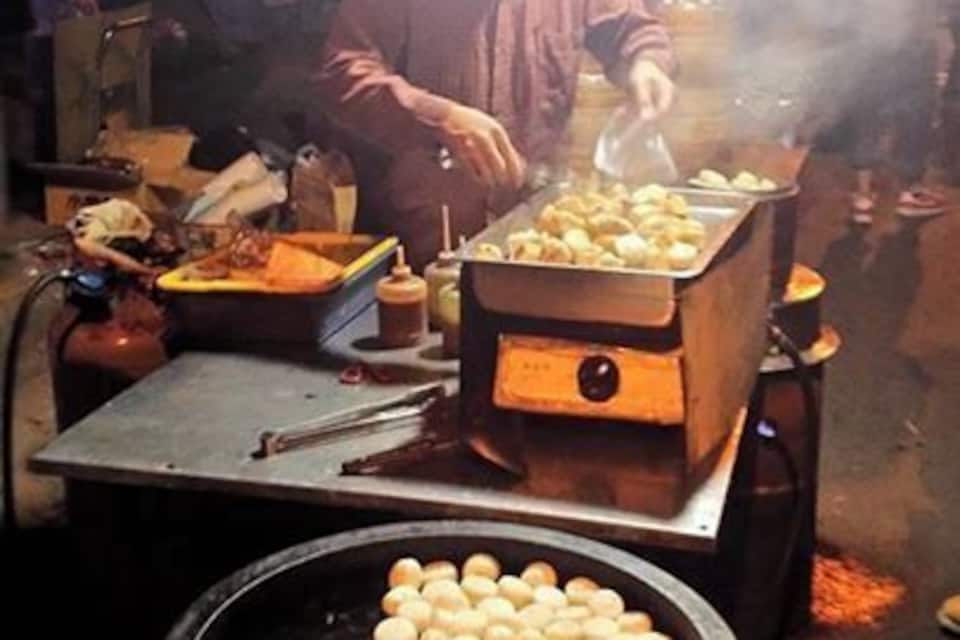 Vendedor de comida de rua cozinhando em uma churrasqueira, com uma panela grande de comida e uma bandeja de itens.