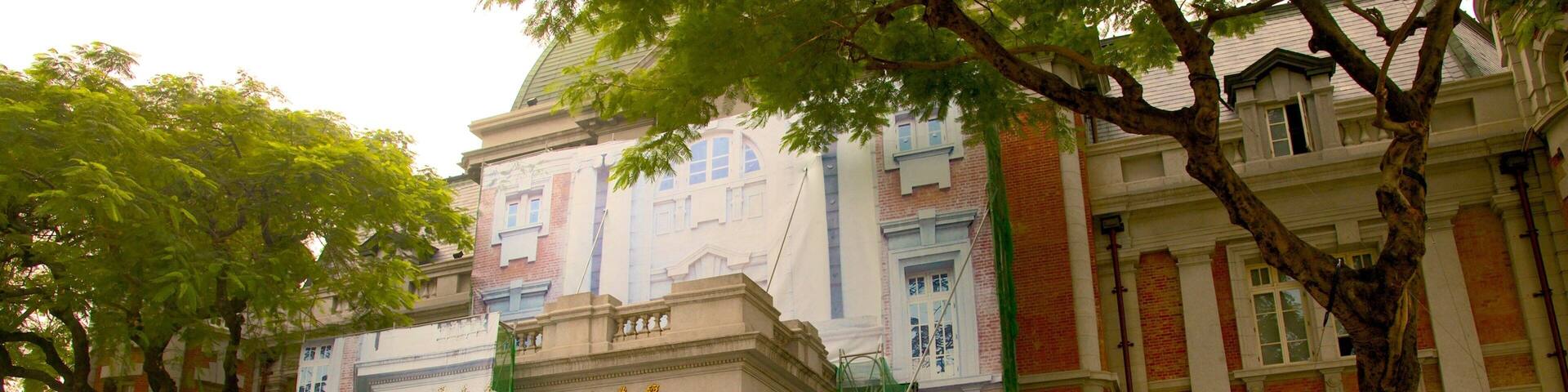 A historic building with classical architecture, including columns and a pediment, surrounded by trees and a small garden.