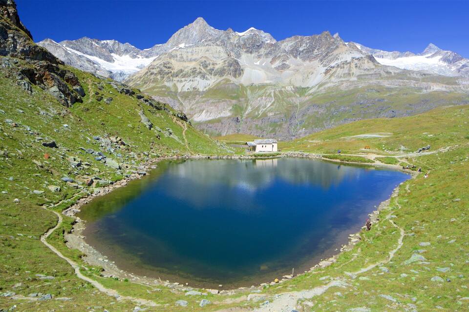 Un lac paisible, entouré de montagnes, une petite cabane et un ciel bleu azur.