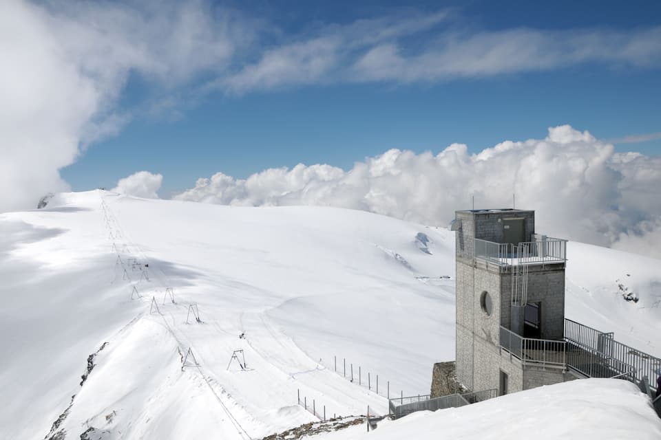 A snow-covered mountain with a stone tower and a ski slope.