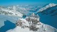 A snow-covered mountain peak with a small observatory and a lake in the valley below.