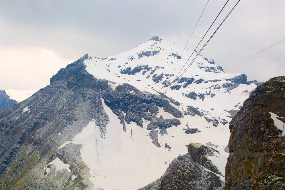 A snow-covered mountain with rocky outcrops and a cable car system.