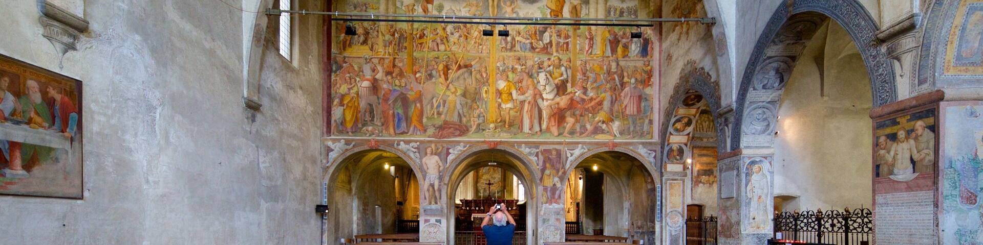 An interior of a church with wooden pews, a large mural on the wall, and a man taking a photo.