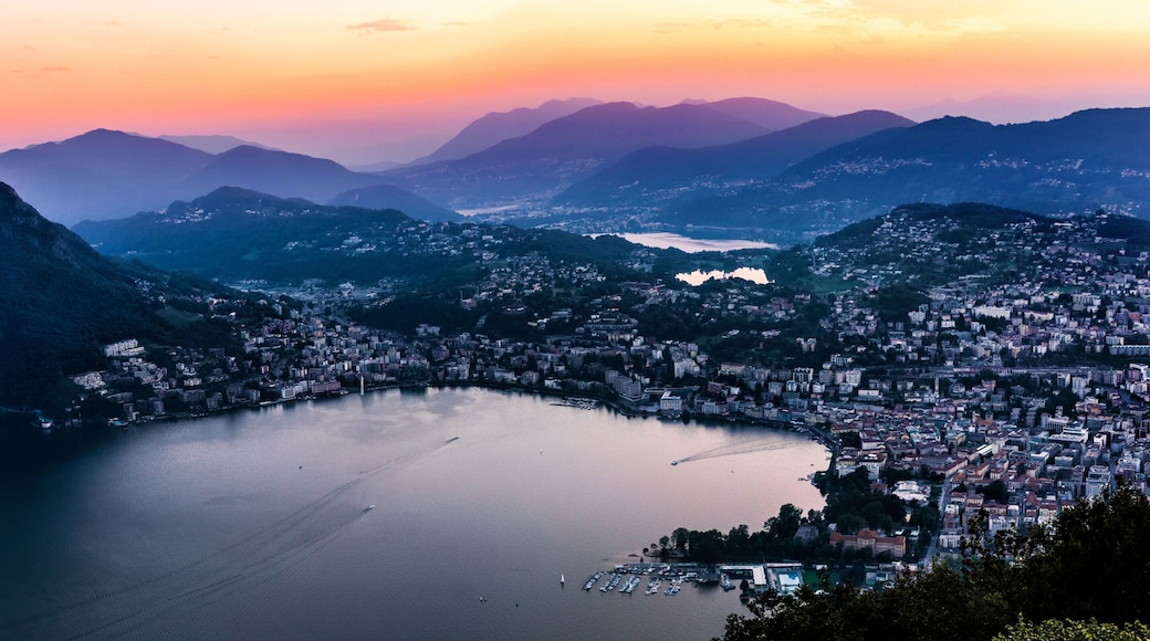 Aerial view of the lake Lugano surrounded by mountains and evening city Lugano on during dramatic sunset, Switzerland, Alps. Travel