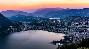 Aerial view of the lake Lugano surrounded by mountains and evening city Lugano on during dramatic sunset, Switzerland, Alps. Travel