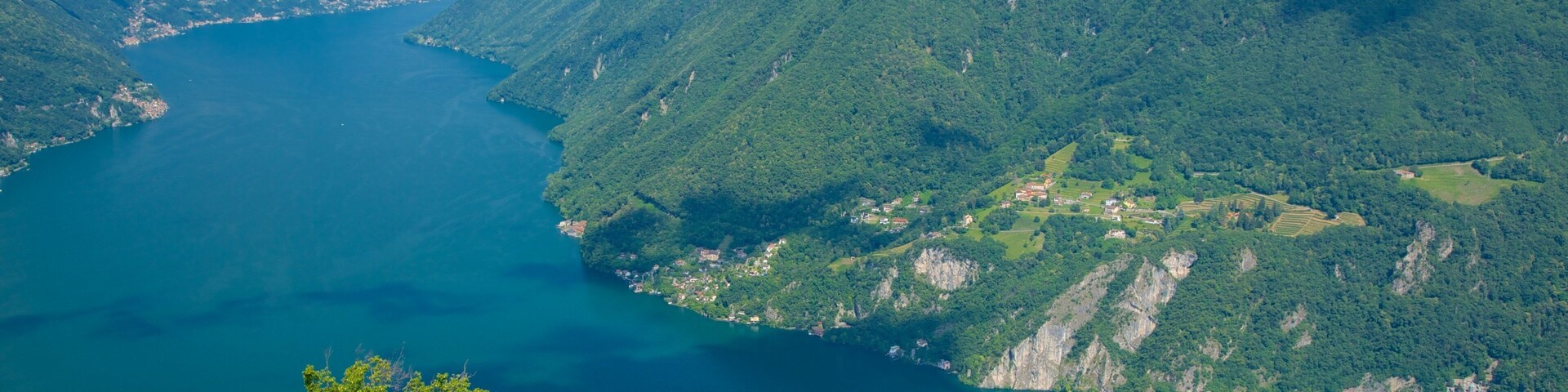 Paisagem montanhosa com um lago rodeado por vegetação exuberante e um pequeno povoado.