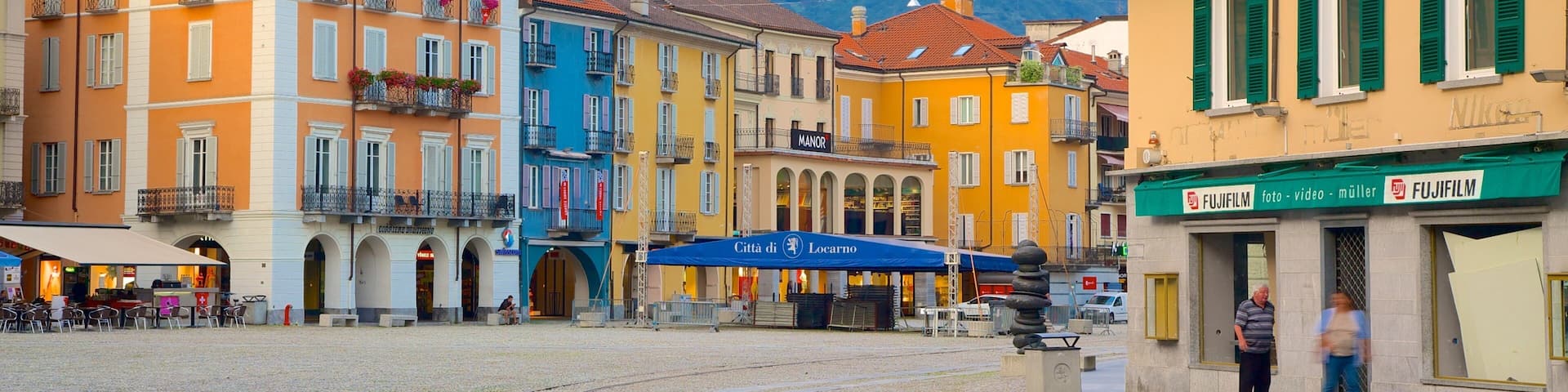 A cobblestone square with colorful buildings, a blue awning, and a mountain in the background.