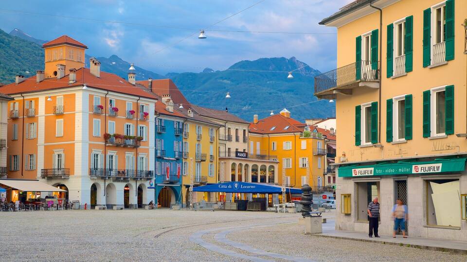 A cobblestone square with colorful buildings, a blue awning, and a mountain in the background.