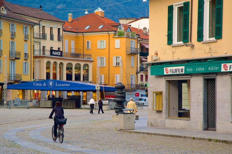 Ein Kopfsteinpflasterplatz mit historischen Gebäuden, einem Radfahrer und einer Statue.