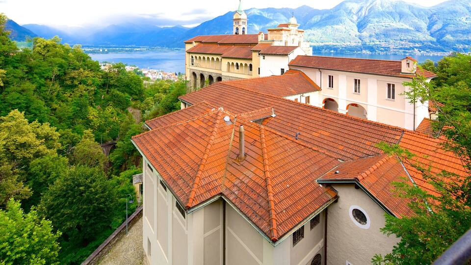 A mountainous landscape with a lake, a church with a red-tiled roof, and lush greenery.