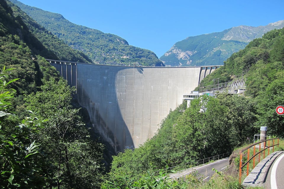 Un grand barrage surmonté d’un pont, entouré de collines verdoyantes et sous un ciel bleu azur.