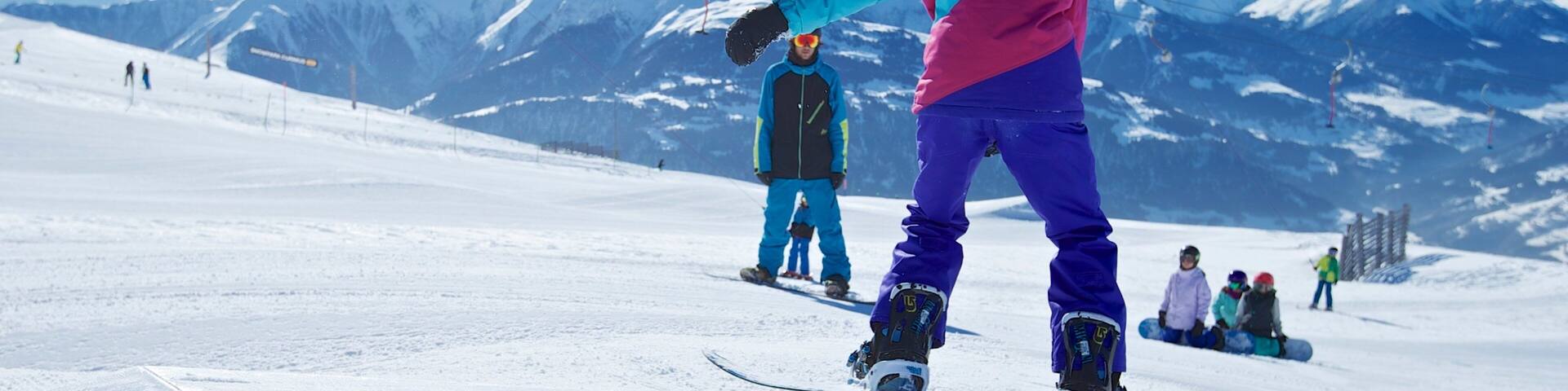 A snowboarder on a green rail at a ski resort with snow-covered mountains in the background.
