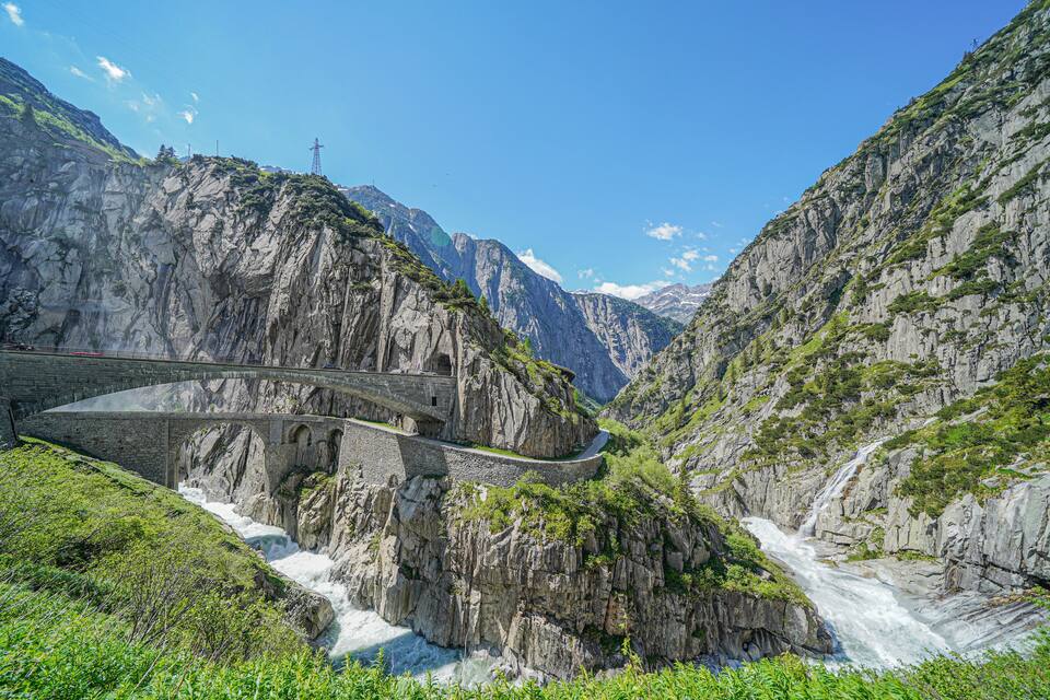 A mountain road winding through a canyon with a bridge over a waterfall.