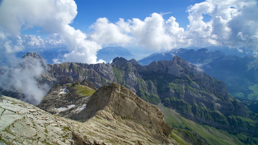 Ein Gebirge mit schroffen Gipfeln, Schneeflecken und einem klaren, blauen Himmel mit Wolken.
