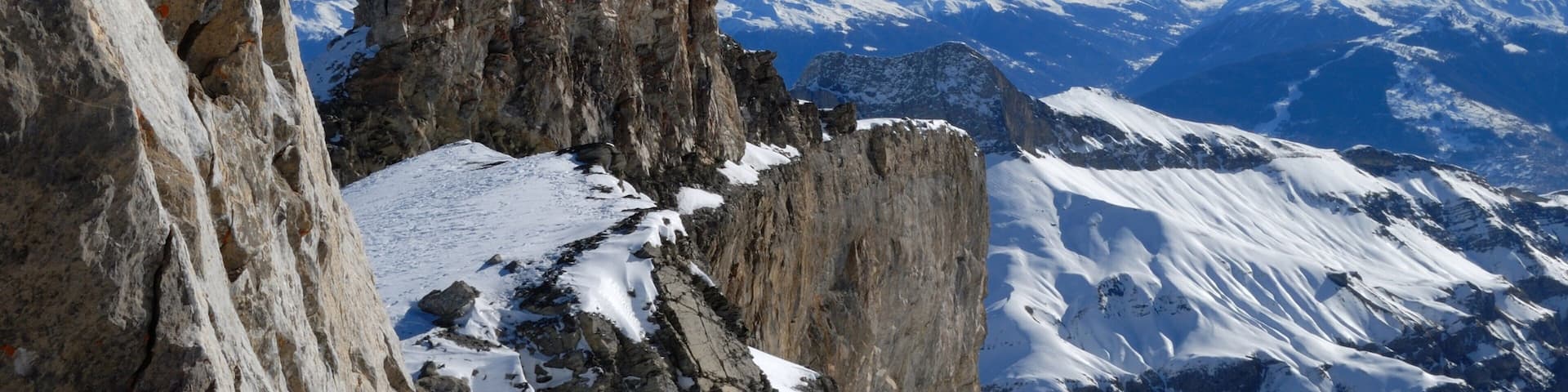 A snow-covered mountain peak with jagged rock formations and a clear blue sky.
