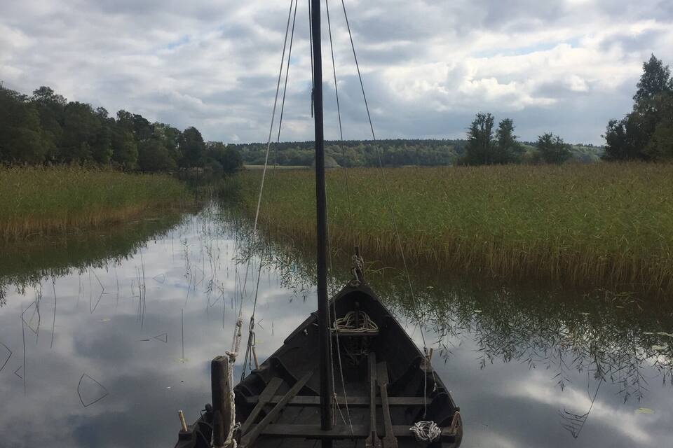 A small wooden boat tied to a dock in a calm river with a cloudy sky above.
