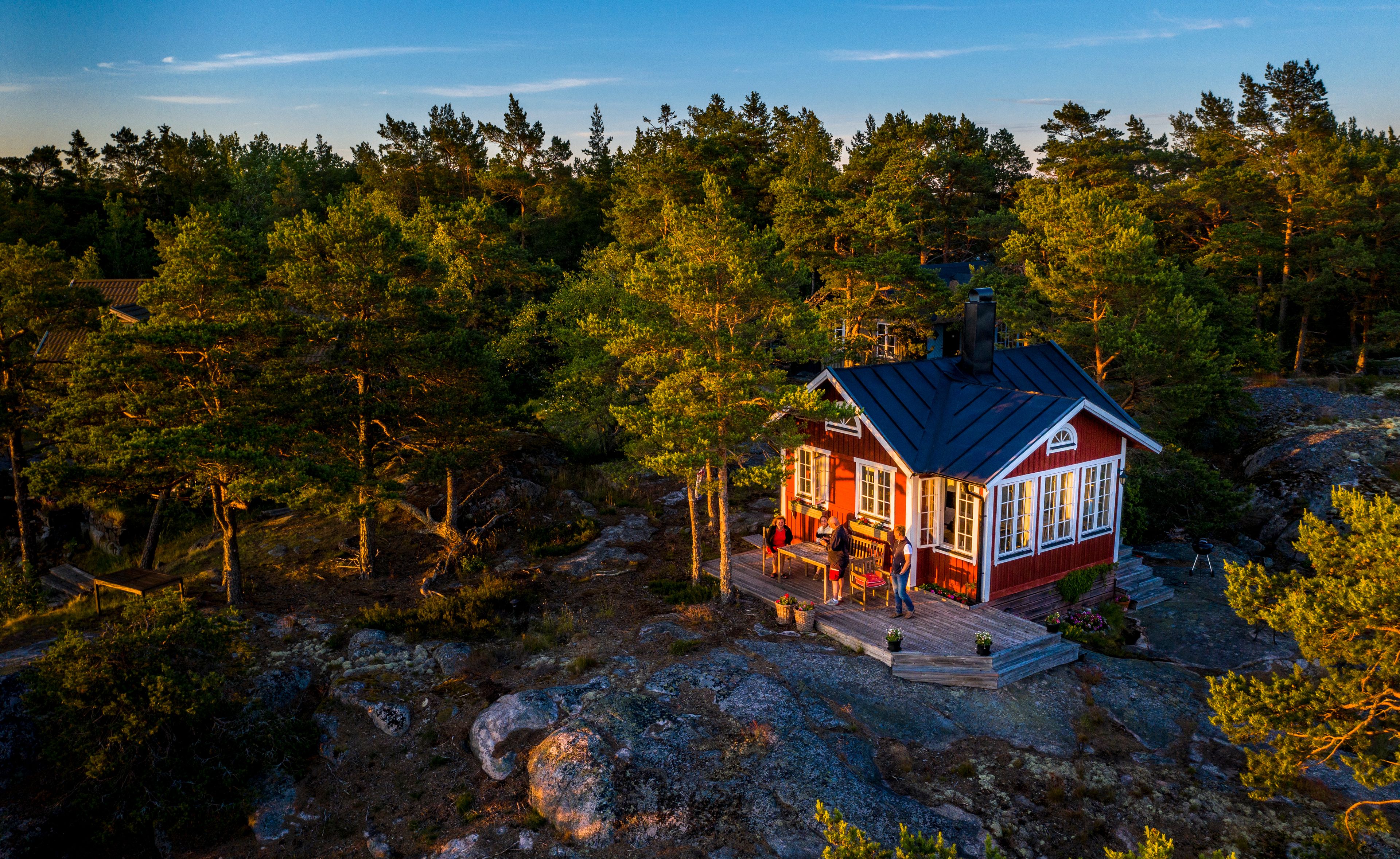 A red cabin with white trim surrounded by dense forest and rocky terrain.