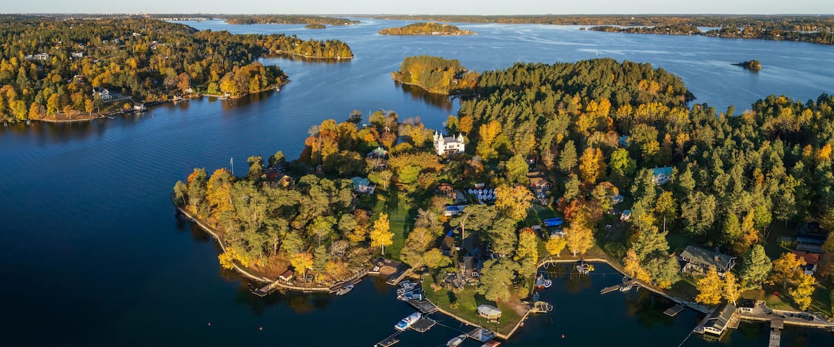 An aerial view of a lake surrounded by dense forests and several islands, with a prominent white building on one of the islands.
