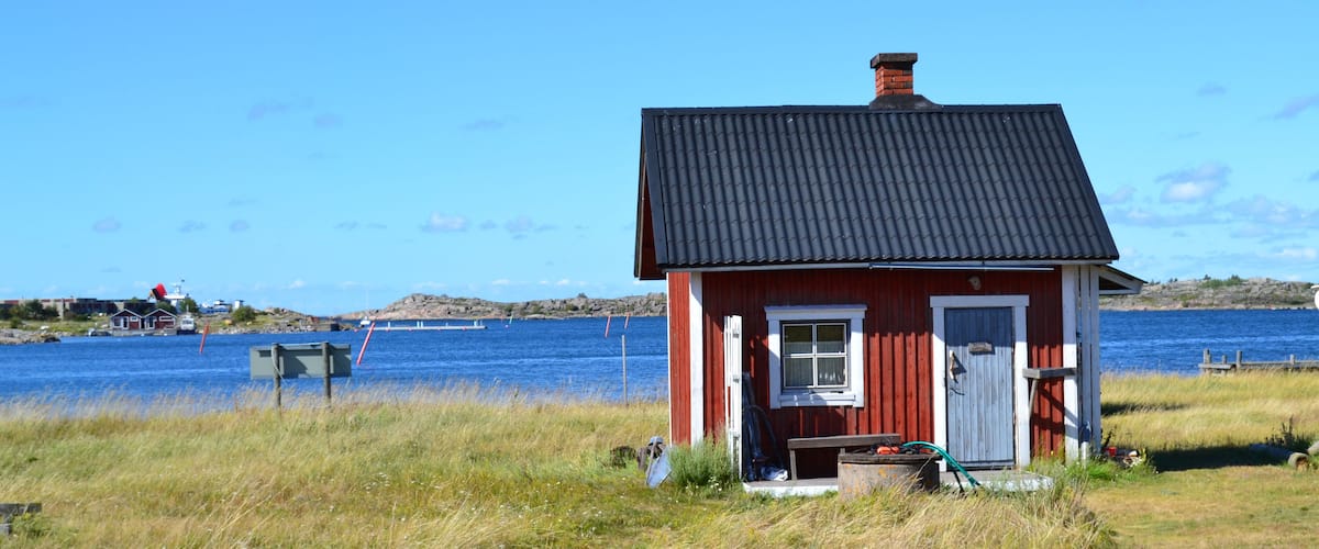 A red wooden house with a black roof by a body of water.