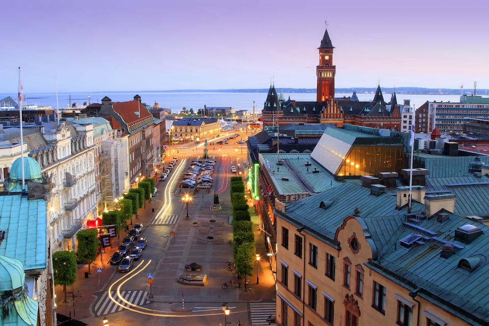 A cityscape with historic buildings, a prominent clock tower, and a waterfront.