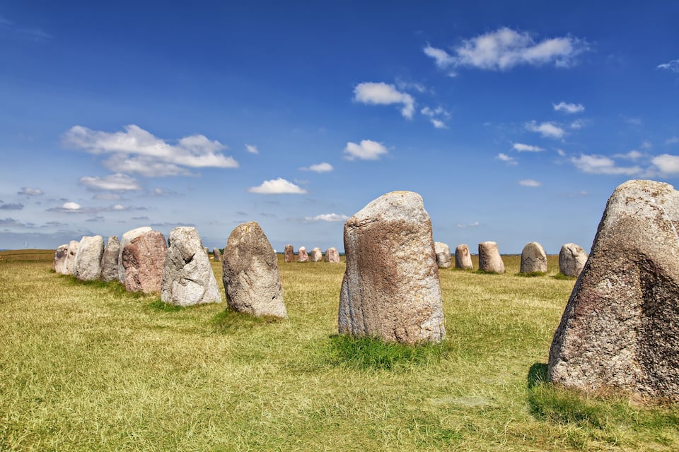 Una fila di menhir in un prato erboso sotto un cielo azzurro limpido.