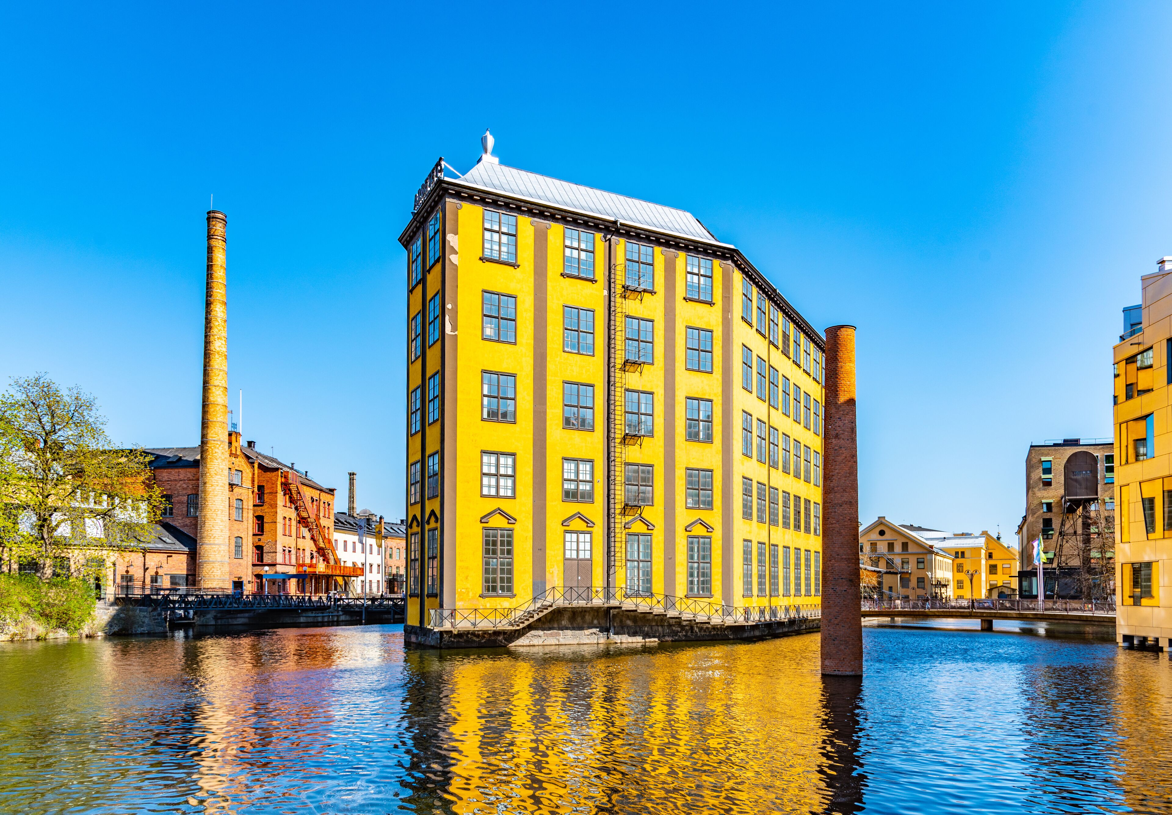 A yellow building with a brick chimney, a bridge, and a river.