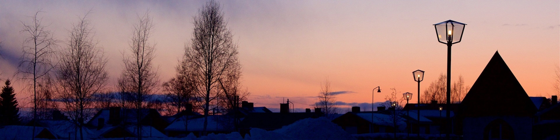 Paisaje nevado con árboles desnudos y casas durante el atardecer.