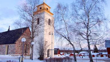 Uma igreja com uma torre alta, um edifício de pedra e casas cobertas de neve.
