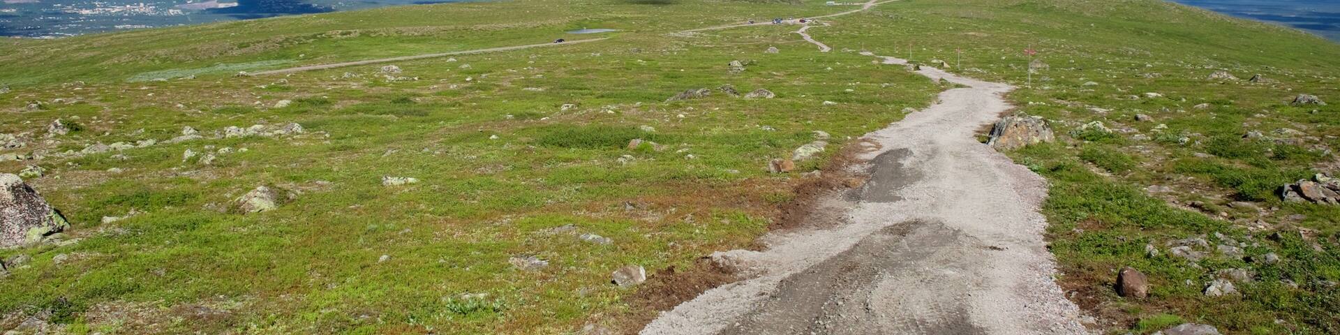 Una colina cubierta de hierba con un sendero de tierra, un edificio lejano y una torre.