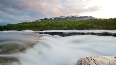 A river flowing over a rocky surface with a forested hillside and a mountain in the background.