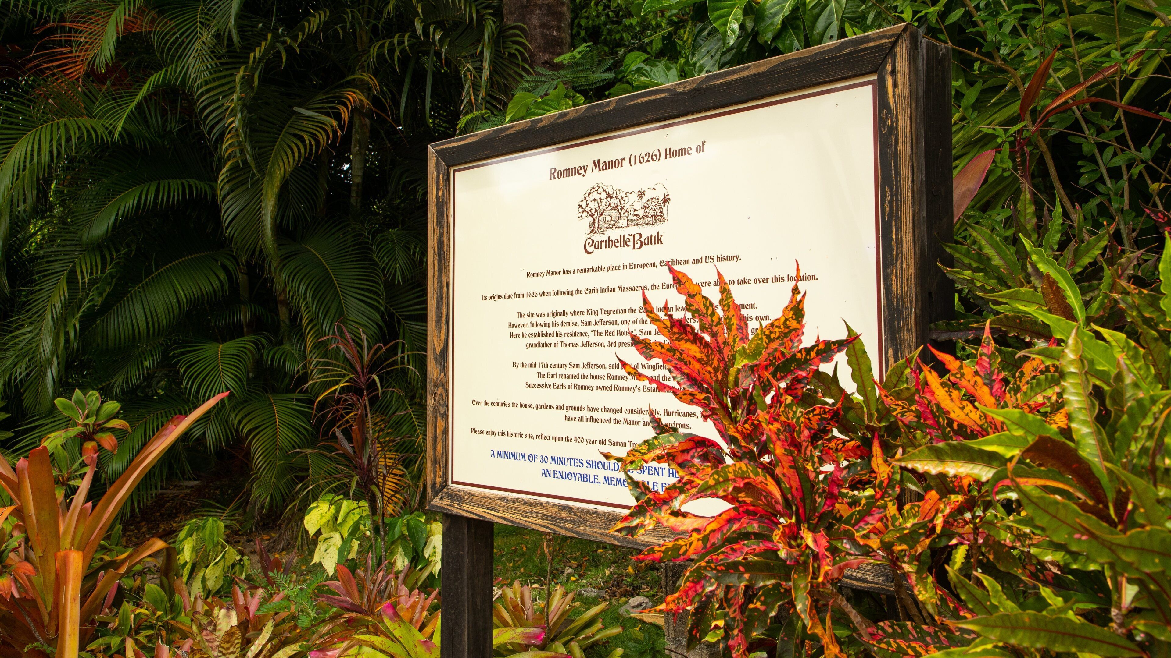 Un cartel histórico sobre Romney Manor (1626) en un jardín exuberante.
