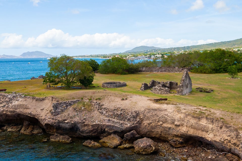 A coastal landscape with rocky outcrops, a clear blue sea, and distant hills.