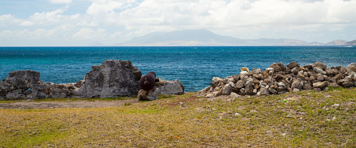 A rocky shoreline with a clear blue sea and distant mountains.