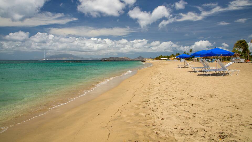A beach with clear turquoise water, footprints in the sand, and blue umbrellas.