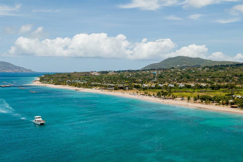 A coastal town with a beach, clear turquoise waters, and a boat in the distance.
