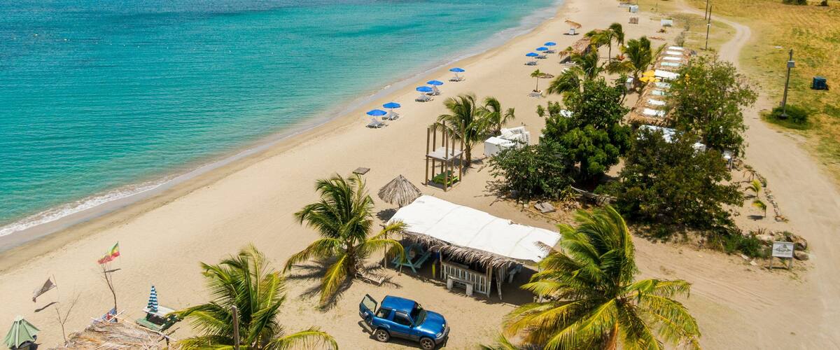 A beach with clear turquoise waters, a row of beach umbrellas, and a few boats in the distance.