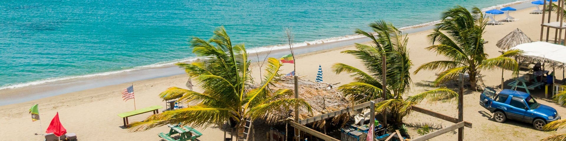 A beach with palm trees, a wooden structure, and a blue car.