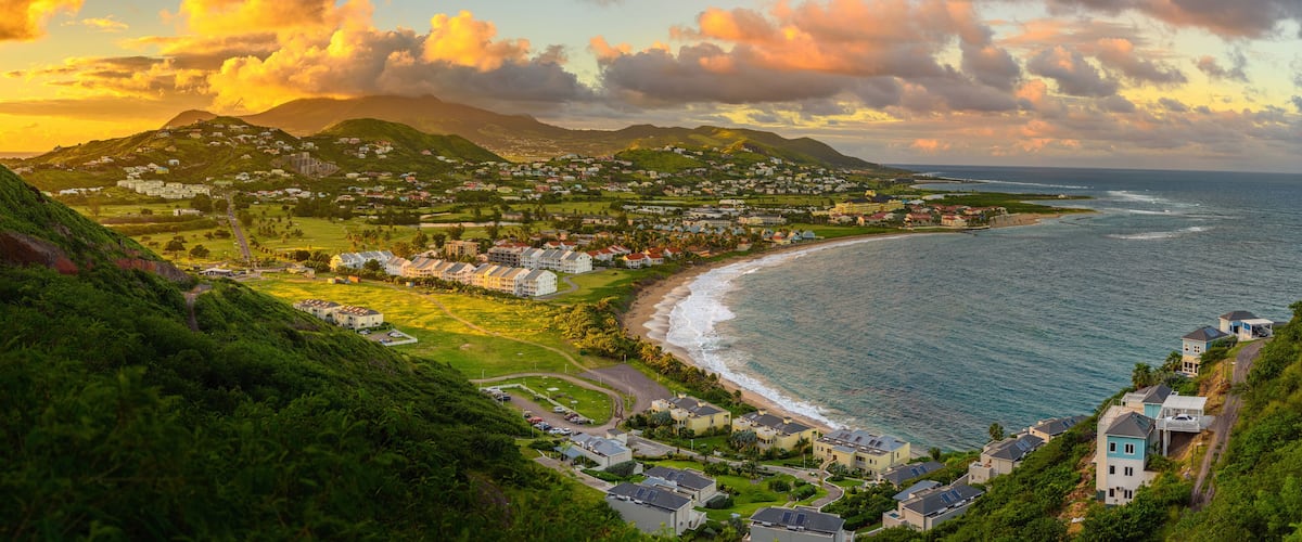 Un pueblo costero con una playa, casas y montañas al fondo.