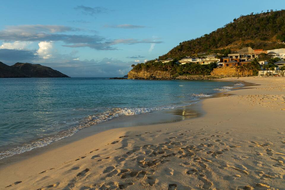 A beach with footprints in the sand, a calm sea, and a mountain in the background.