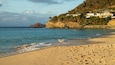 A sandy beach with footprints, calm sea, and houses on a hillside.