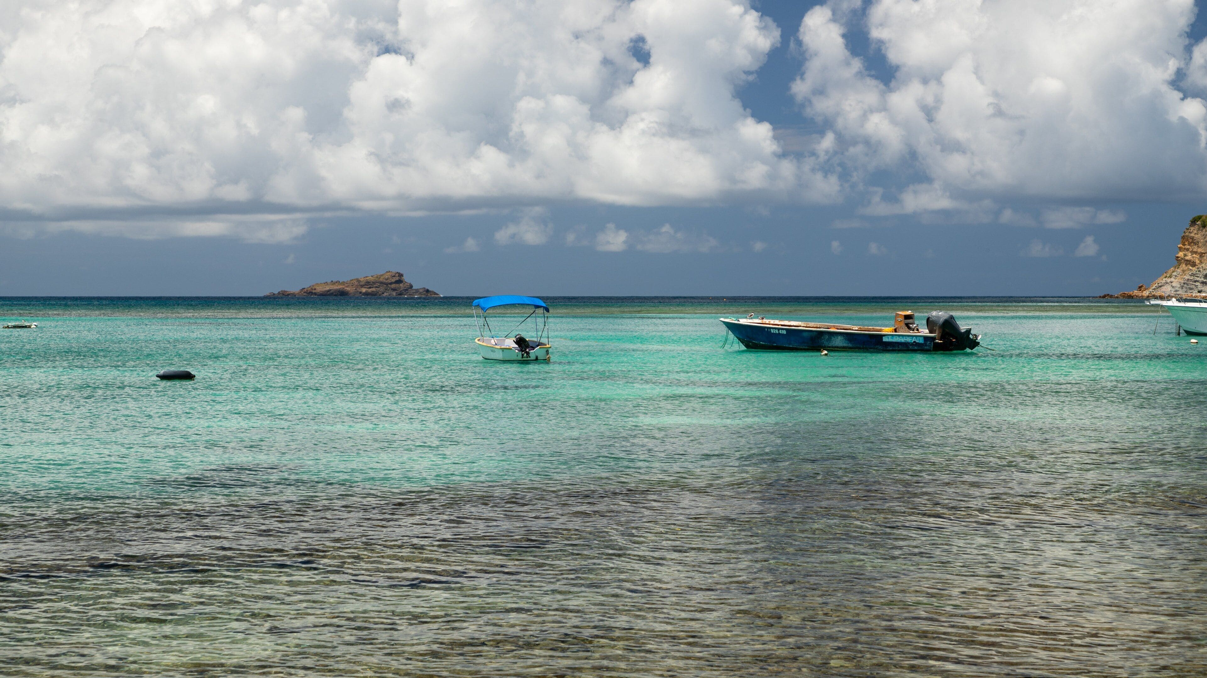 A turquoise sea with boats, a rocky island, and a clear sky.