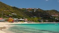 A beach with turquoise waters, a sandy shore, and houses on a hillside.