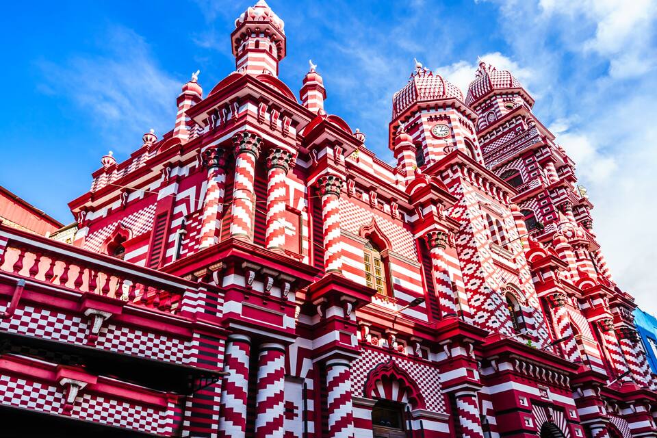 Um edifício com padrão vermelho e branco, com várias cúpulas e detalhes arquitetônicos elaborados.