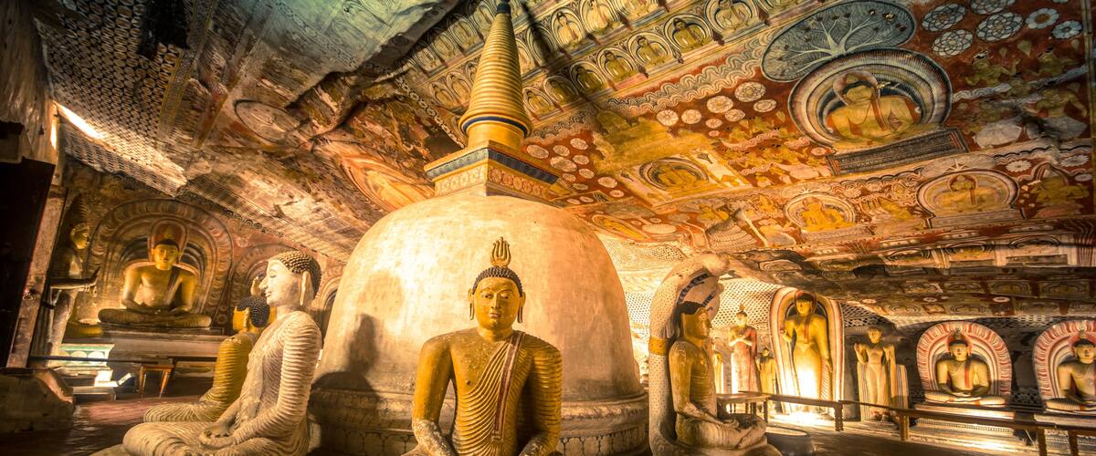 A temple interior with large Buddha statues, intricate ceiling artwork, and a central stupa.