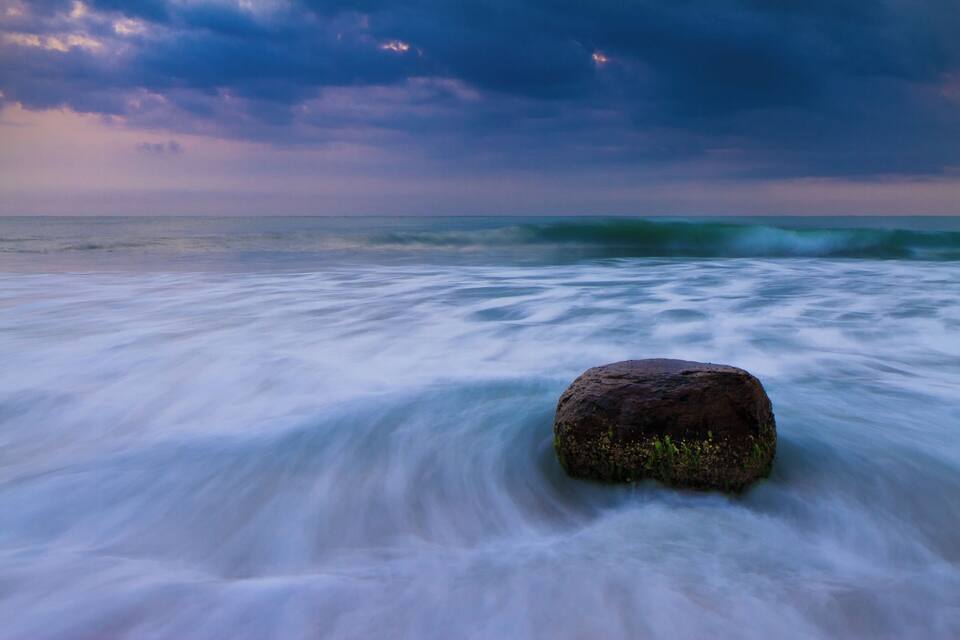 A rock in the ocean with waves around it.