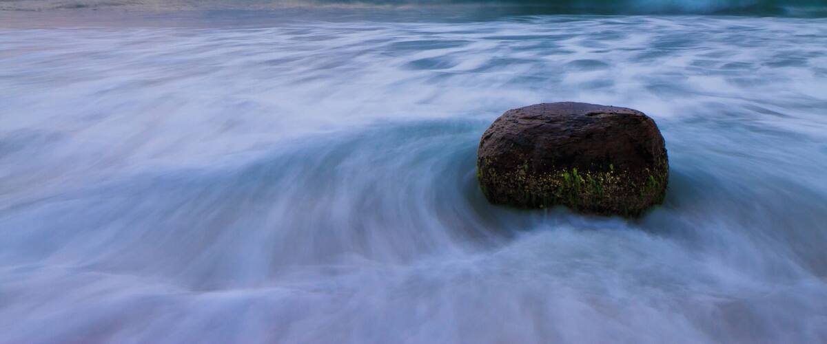 A rock in the ocean with waves around it.
