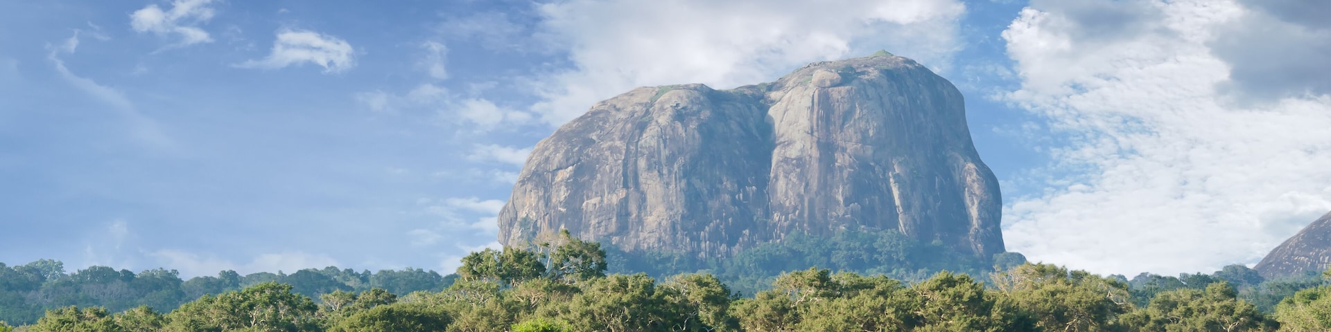 A large rock formation surrounded by lush greenery and a river.