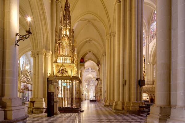 Interior de catedral com altos tetos abobadados, lustres elaborados e piso xadrez.